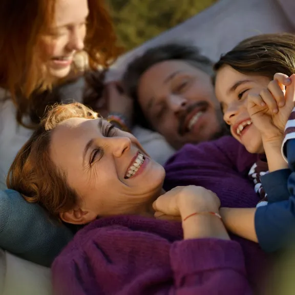 Eine Familie mit zwei Kindern liegt vergnügt in einer Hängematte.