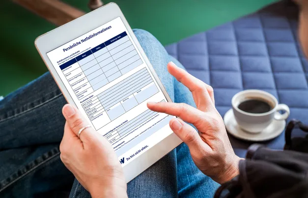 Eine Seite des Notfallordners ist auf einem Tablet geöffnet. Eine Person hält das Tablet in der Hand.