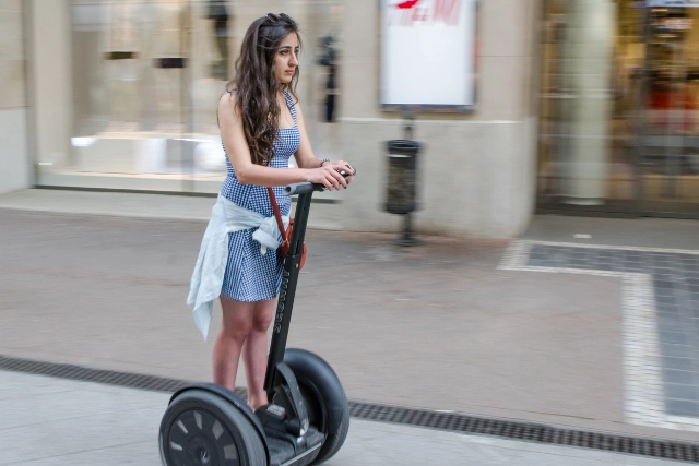 Frau auf Segway in urbaner Fußgängerzone mit Geschäften im Hintergrund