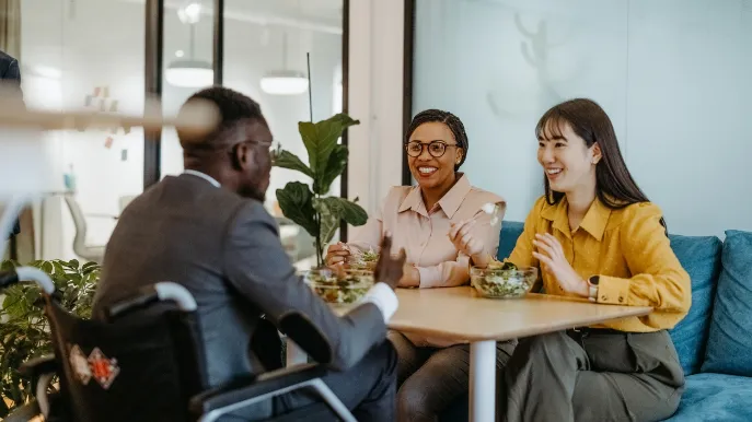 Drei Arbeitskollegen und Arbeitskolleginnen essen zusammen in der Kantine.