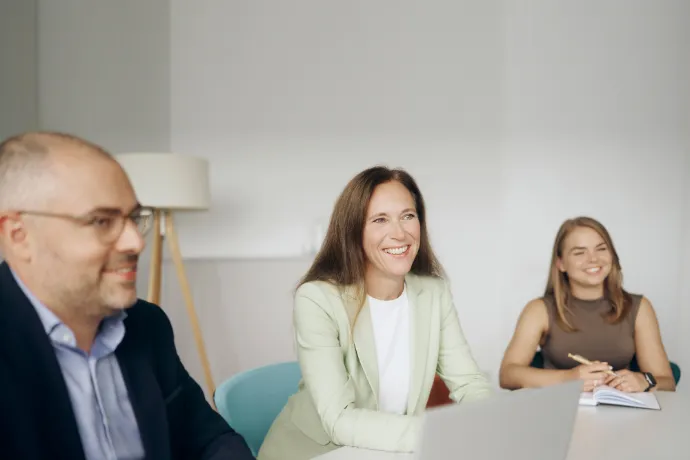 Drei Personen in Businesskleidung sitzen in einem Büro vor einem Notebook und führen ein Gespräch.