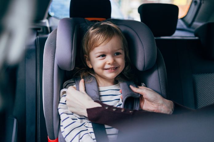 Ein Mädchen sitzt im Auto im Kindersitz und wird angeschnallt.