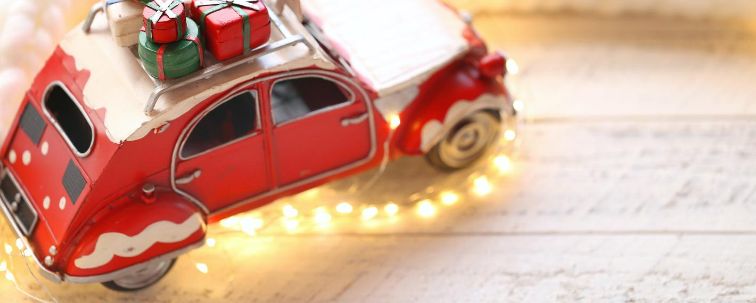 Weihnachtsauto mit Geschenken, Lichterkette und weißem Strickschal im Hintergrund.