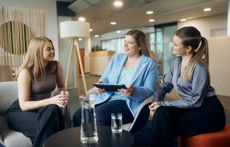 Drei Kolleginnen sitzen zusammen und unterhalten sich mit einem Tablet in der Hand.