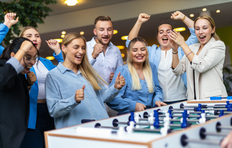 Jubelnde Nachwuchskräfte spielen gemeinschaftlich Tischfußball und genießen eine entspannte Pause in einem modernen Büro.