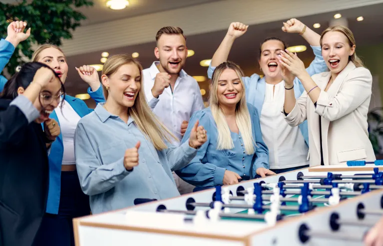 Jubelnde Nachwuchskräfte spielen gemeinschaftlich Tischfußball und genießen eine entspannte Pause in einem modernen Büro.