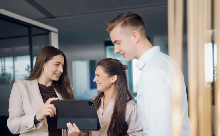 Drei dualer Studentinnen und Studenten tauschen sich an einem Tablet aus.