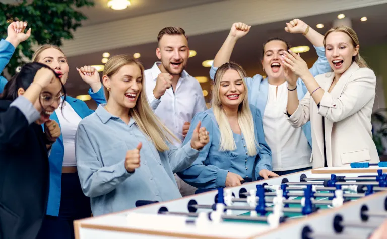 Jubelnde Nachwuchskräfte spielen gemeinschaftlich Tischfußball und genießen eine entspannte Pause in einem modernen Büro.
