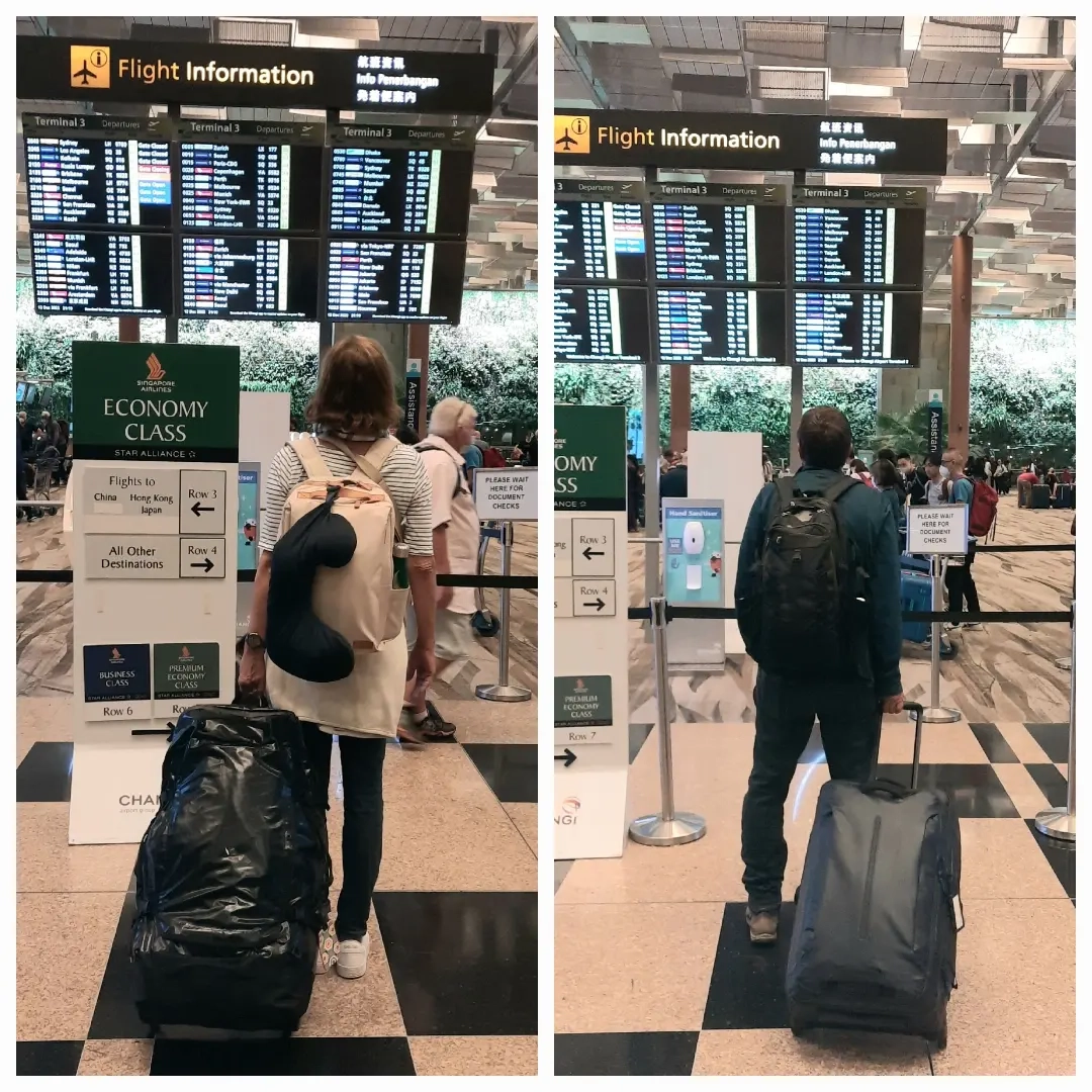 Reisende mit Gepäck warten am Gate im Flughafenterminal unter Anzeigetafeln mit Flugdaten und Abflugzeiten