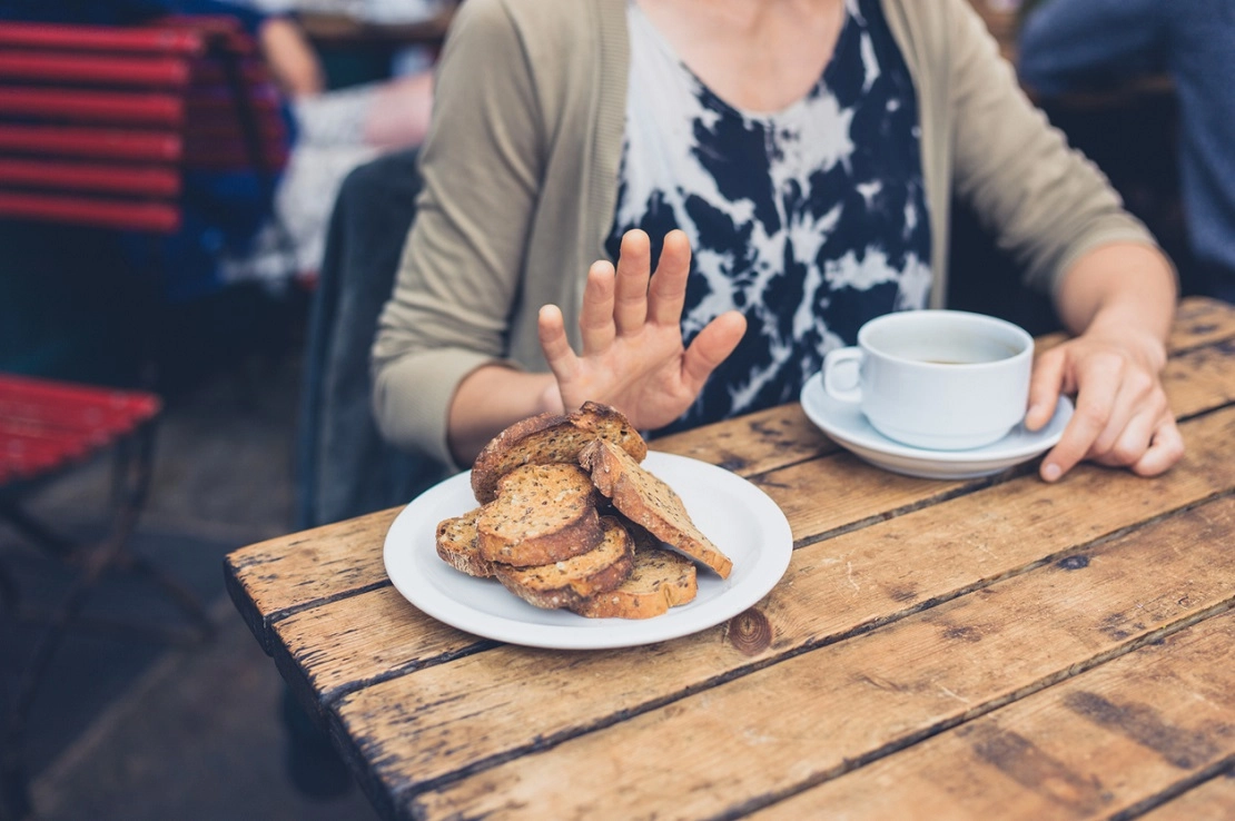 Frau lehnt Toastbrot ab und hält Kaffeetasse an rustikalem Holztisch in Café