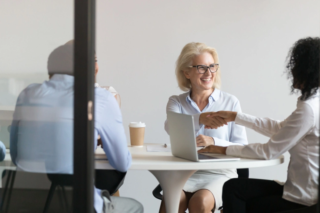 Drei Geschäftsfrauen in einem Büro besprechen ein Projekt, eine sitzt am Laptop, die andere zeigt auf den Bildschirm.