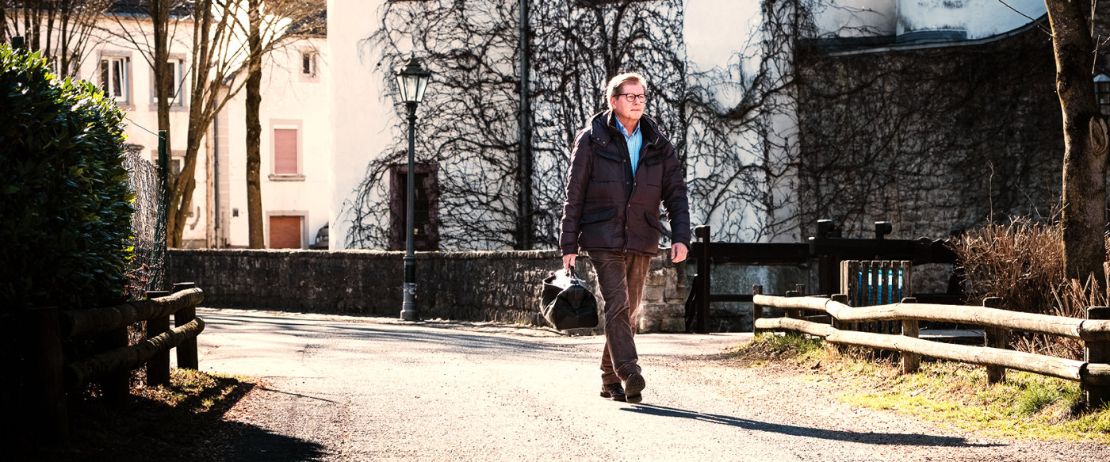 Landarzt mit Arzttasche geht eine Straße entlang.