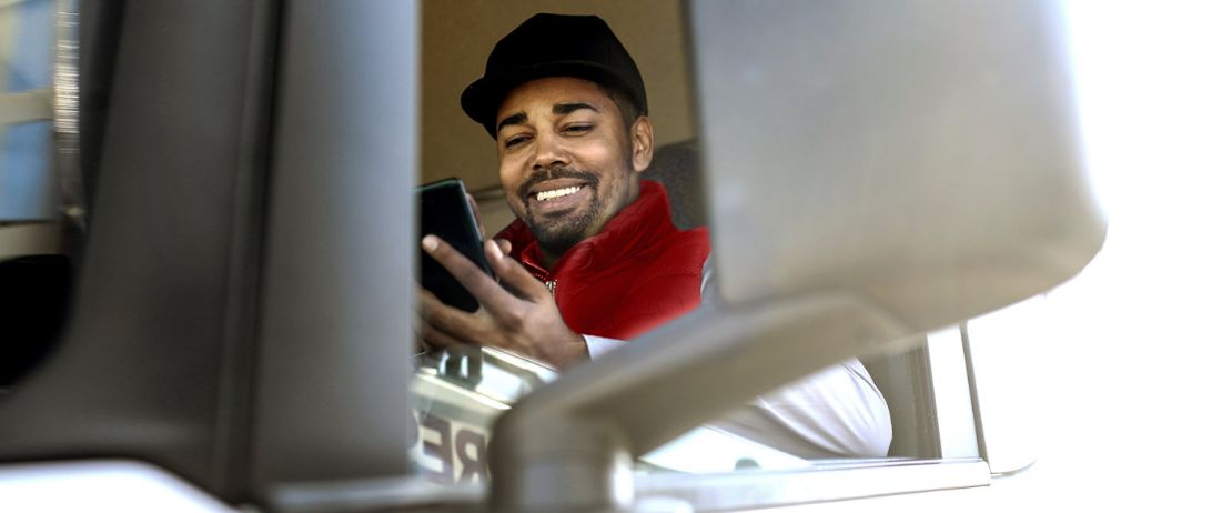 Truck-Fahrer im Truck, schaut auf sein Smartphone.