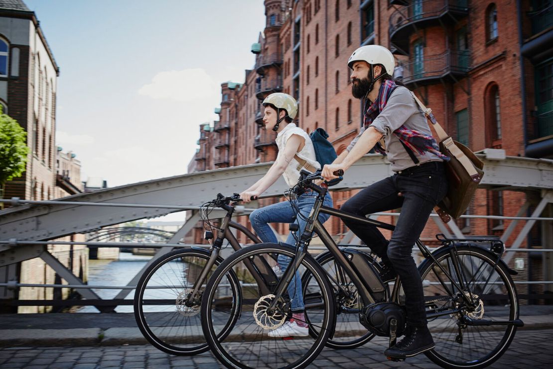 Zwei Personen fahren mit e-bike durch Stadt.