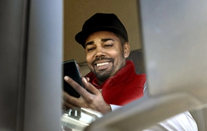 Mann mit schwarzer Mütze und rotem Schal hält lächelnd sein Smartphone in die Kamera
