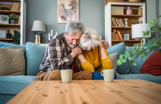 Ehepaar umarmt sich trotz Sorgen und Unstimmigkeiten auf der Couch.