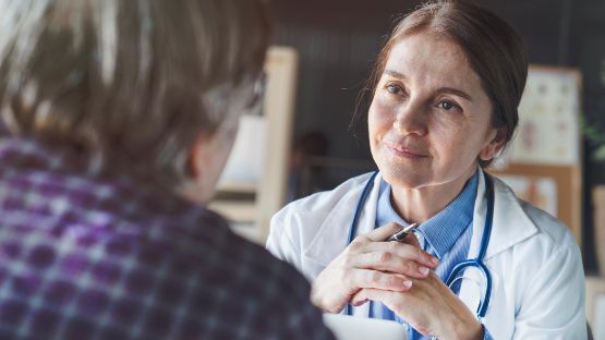 Verstaendnisvoll lächelnde Aerztin sieht grauhaarigen Mann direkt an