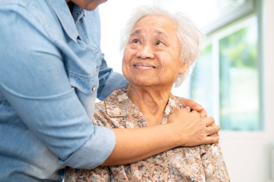 Pflegebeduerftige weisshaarige Frau wird liebevoll von Tochter umarmt