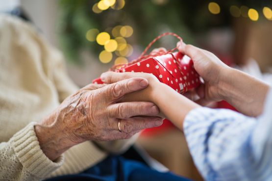 Eine pflegebedürftige Seniorin bekommt ein Weihnachtsgeschenk von ihrer Angehörigen überreicht.
