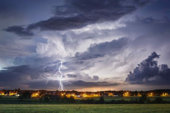 Ein Gewitter mit Blitzen über einer Ortschaft.