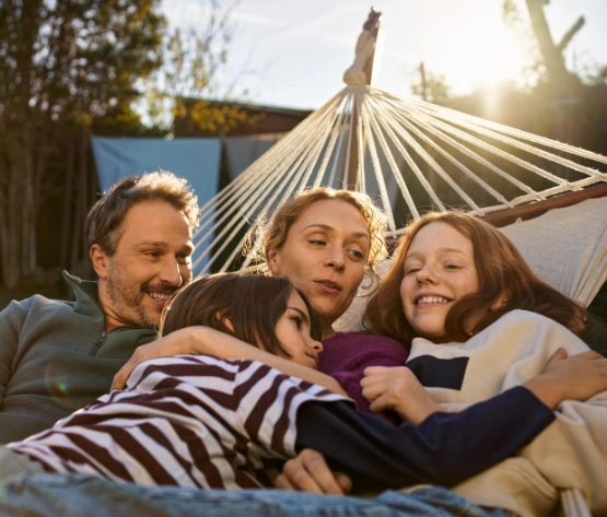 Eine Familie mit Vater, Mutter und zwei Kindern liegt vergnügt in einer Hängematte.