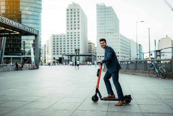 Ein Mann fährt im Anzug auf einem E-Roller durch die Stadt.