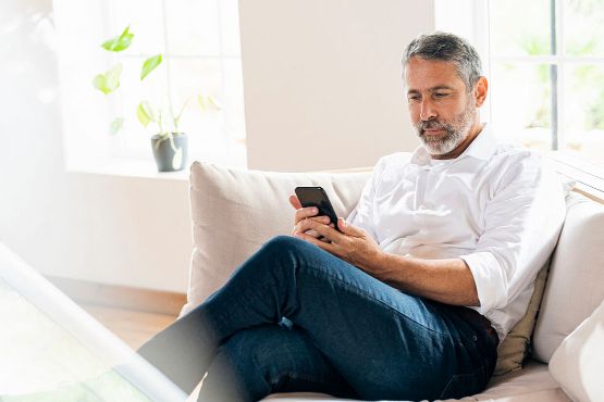 Mann sitzt mit Handy auf einem Sofa