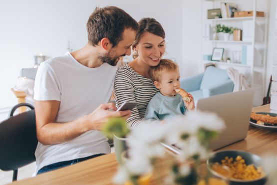 Familie mit Kleinkind sitzt essend vor einem Laptop.