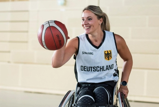 Basketballspielerin in weißem Trikot hält einen roten-weißen Basketball in einer Halle