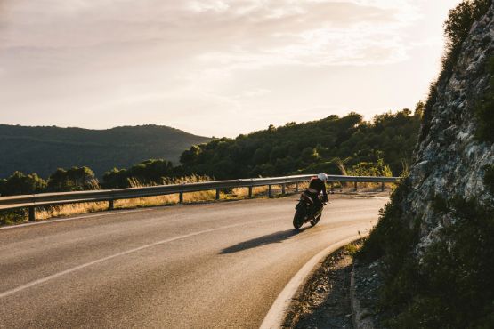 Ein Motorrad fährt auf einer Straße in den Bergen bei Sonnenschein.
