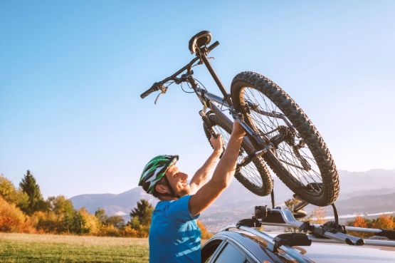 Mann nimmt sein Mountainbike vom Autodach herunter.