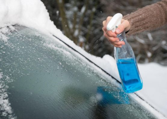 Person enteist die Windschutzscheibe mit Eisfrei-Spray.