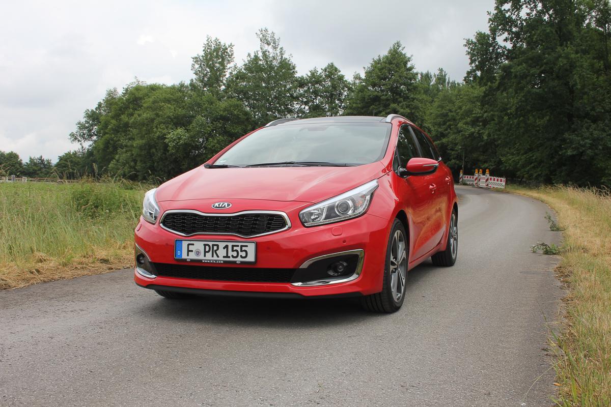 Roter Kia Cee'd auf ländlicher Straße mit Baumreihe und Grünland im Hintergrund