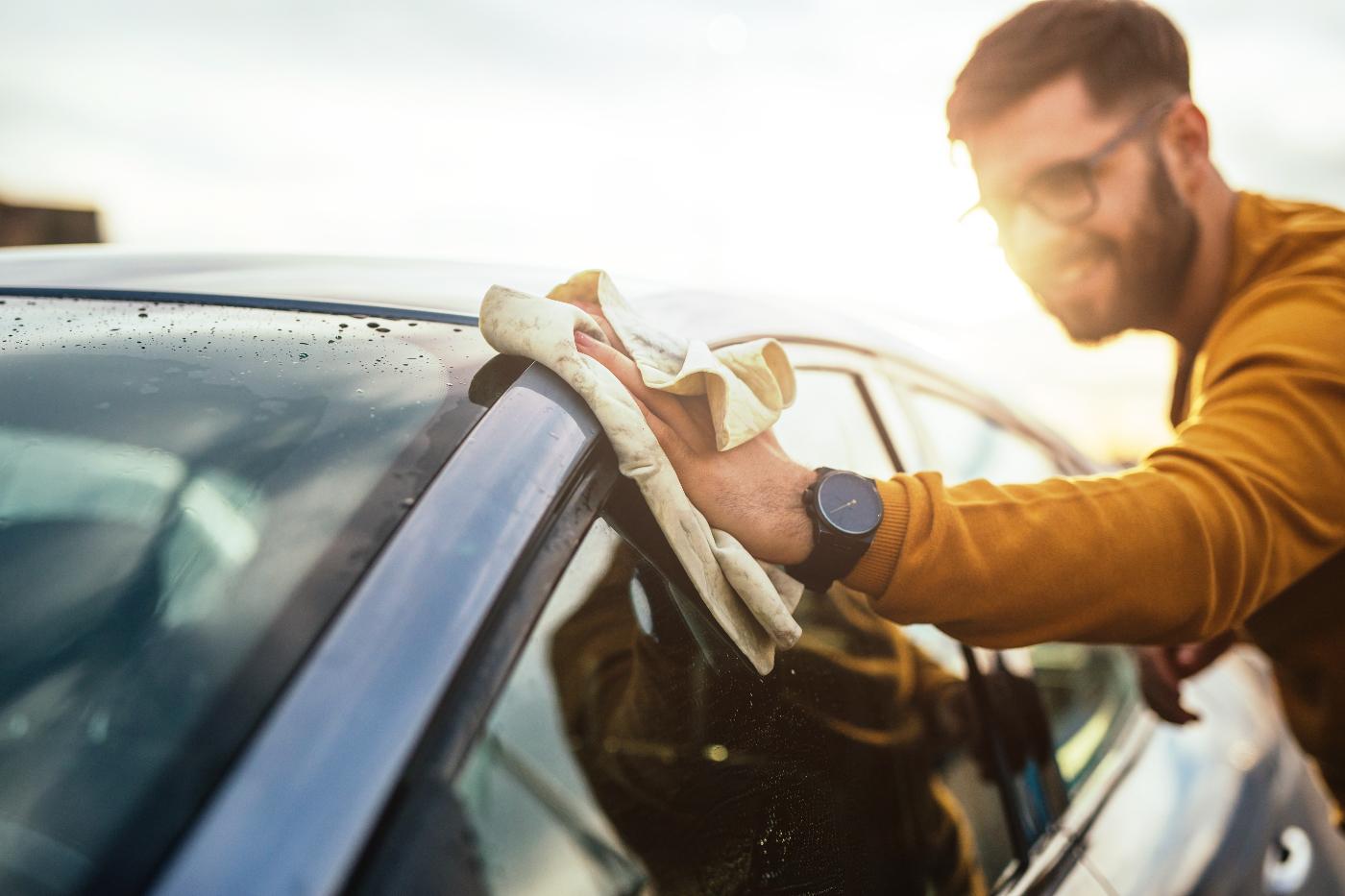 Junger Mann wischt das Dach seines Autos mit einem Mikrofasertuch sauber.