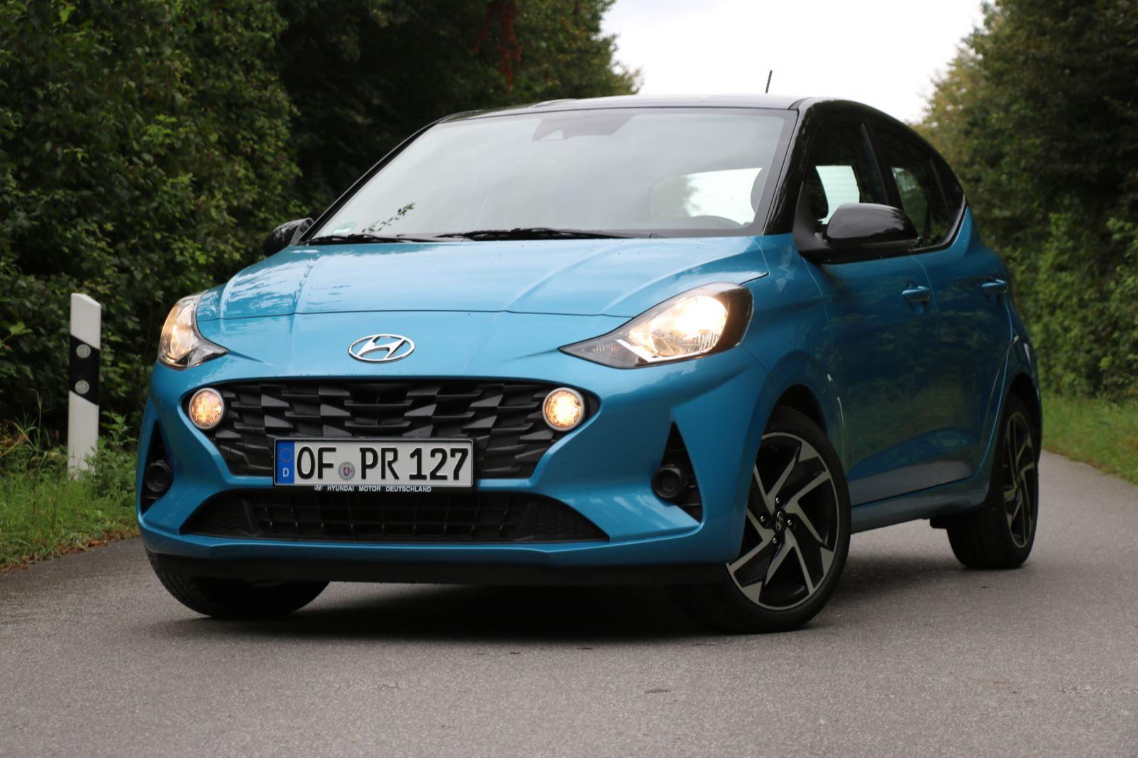 Blauer Hyundai i10 mit Kennzeichen auf Landstraße, umgeben von grünen Bäumen