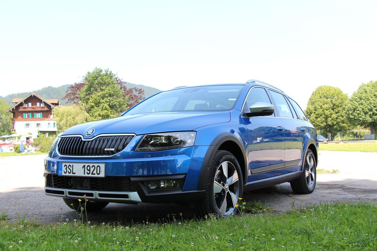 Blauer SUV steht auf grüner Wiese vor Haus und Bäumen, sonniger Sommertag
